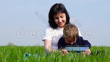 母亲和<strong>孩子</strong>花时间坐在绿草上，在平板电脑上<strong>看孩子</strong>们`电影。